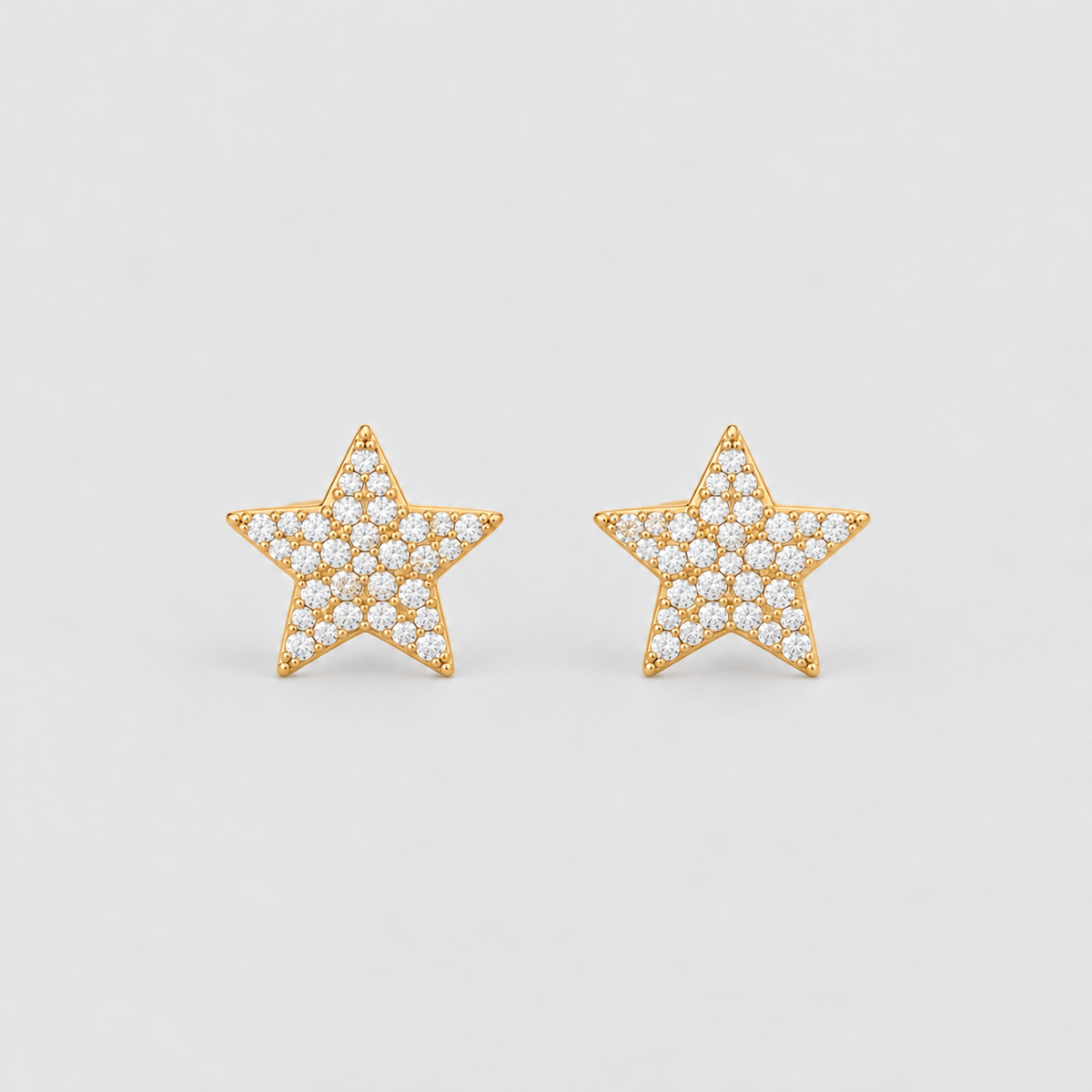 A pair of gold star-shaped stud earrings paved with small clear stones, set against a plain light gray background.
