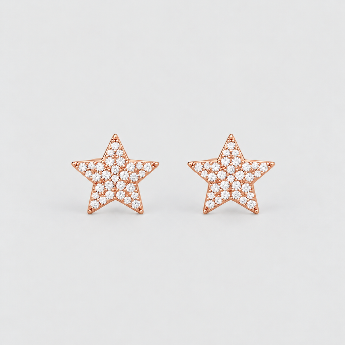 A pair of rose gold star-shaped stud earrings paved with small clear gemstones, set against a clean light gray background.