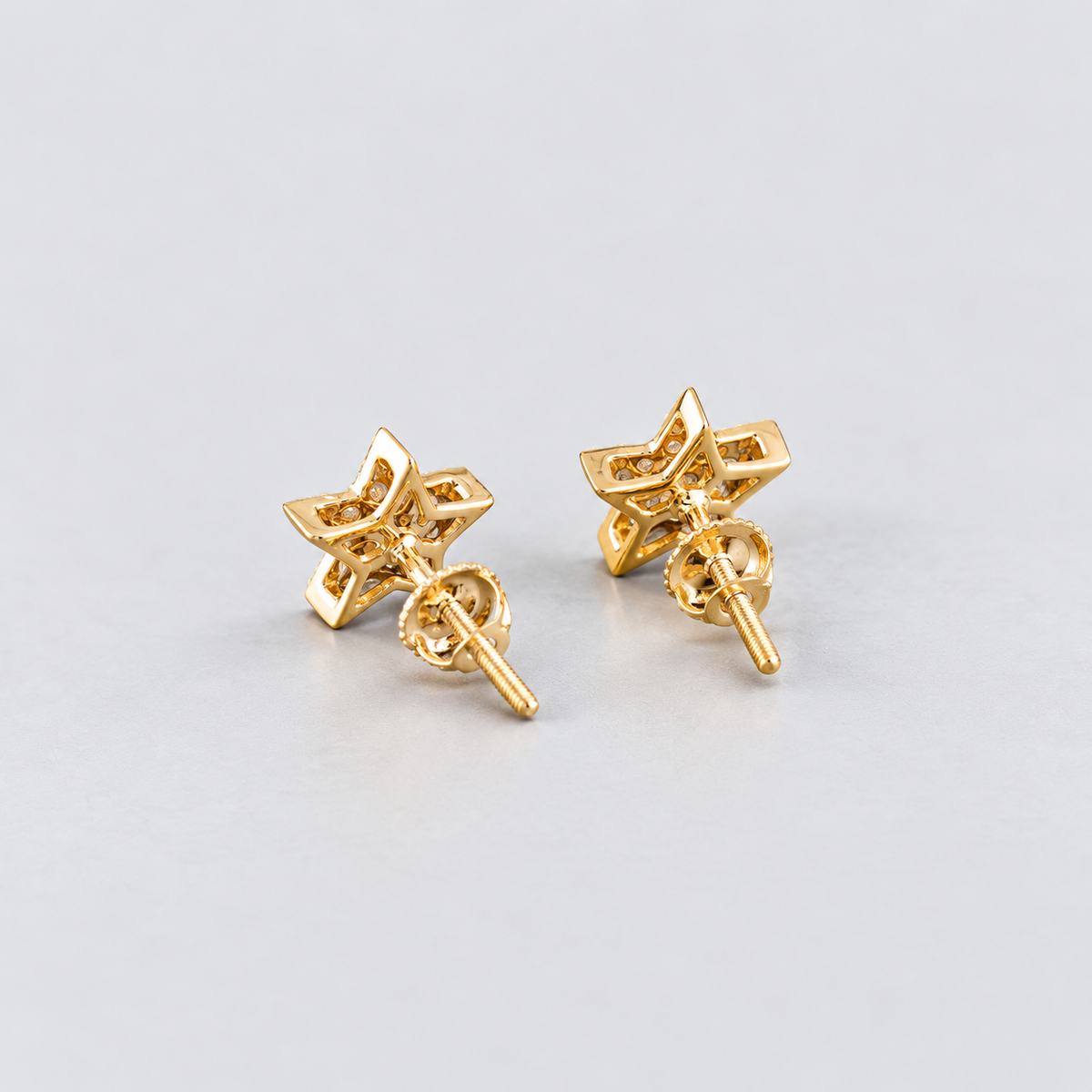 A pair of gold star-shaped stud earrings with butterfly backings, shown on a light gray background.
