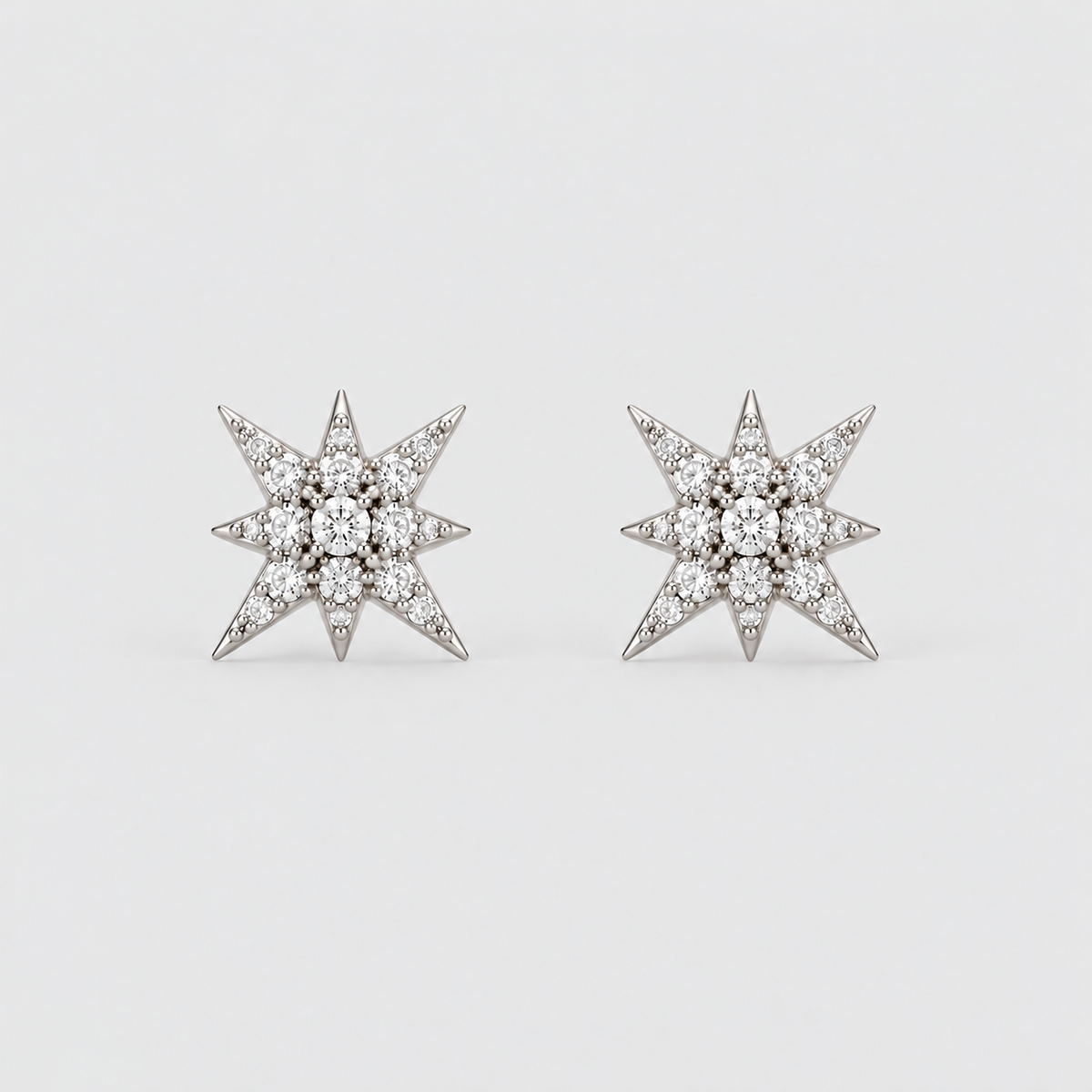 A pair of star-shaped stud earrings set with clear gemstones in a silver-toned metal, displayed on a clean, light gray background.