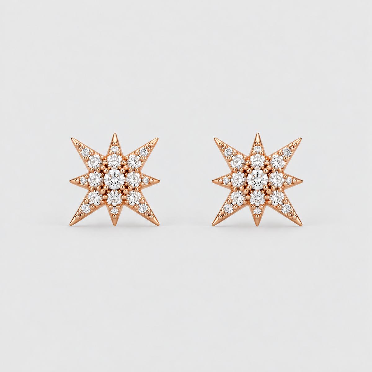 A pair of rose gold starburst stud earrings set with round diamonds, displayed on a clean light gray background.