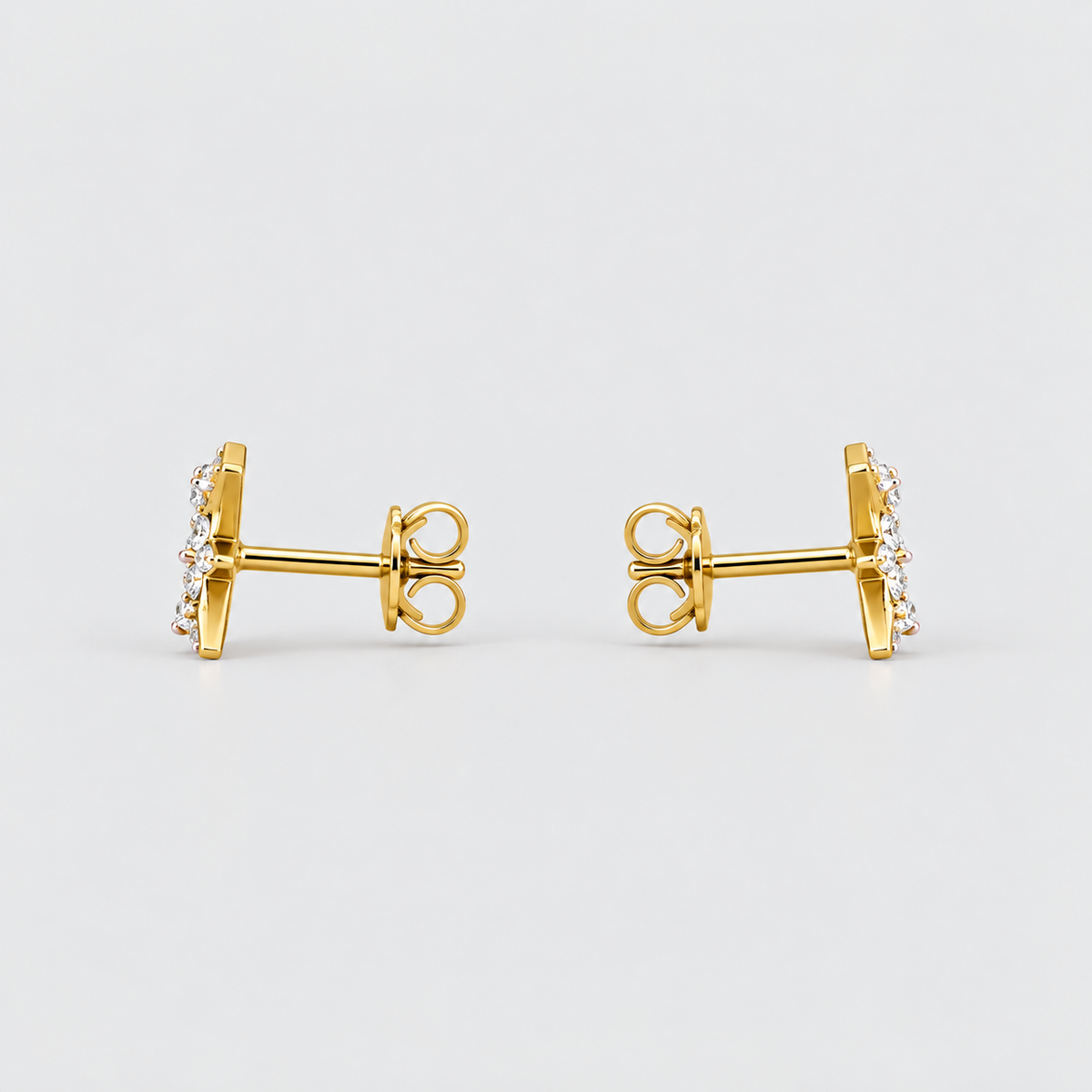 A pair of gold post earrings with a small cluster of clear stones on the front, shown from the side against a light gray background.