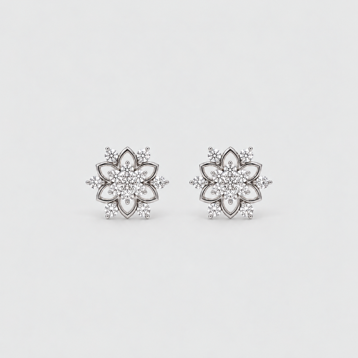 A pair of silver-toned flower-shaped stud earrings set with clear gemstones, displayed on a clean, light gray background.