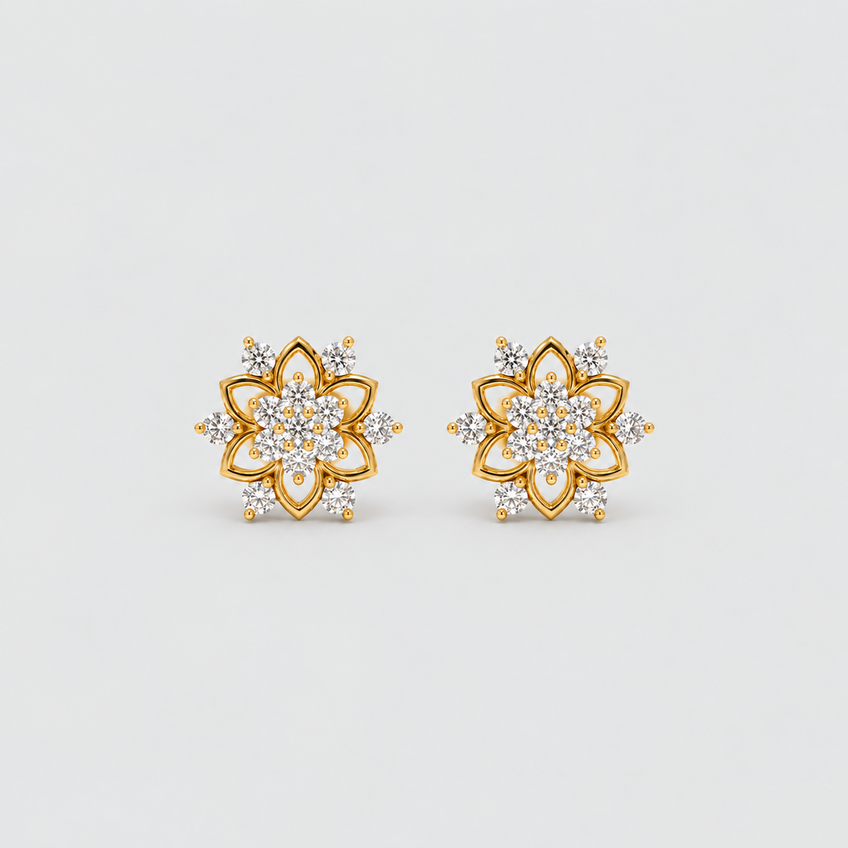 A pair of gold flower-shaped stud earrings set with clear gemstones, displayed on a clean light gray background.