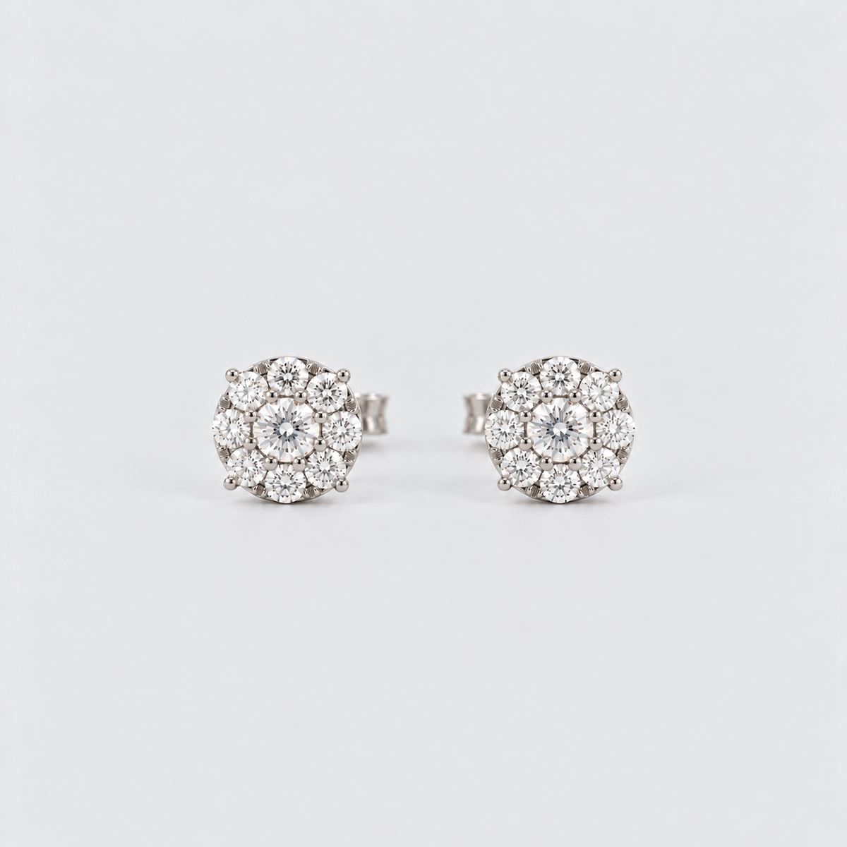 A pair of round cluster stud earrings featuring a central clear gemstone surrounded by multiple smaller clear stones in a silver-toned setting, photographed on a clean light gray background.