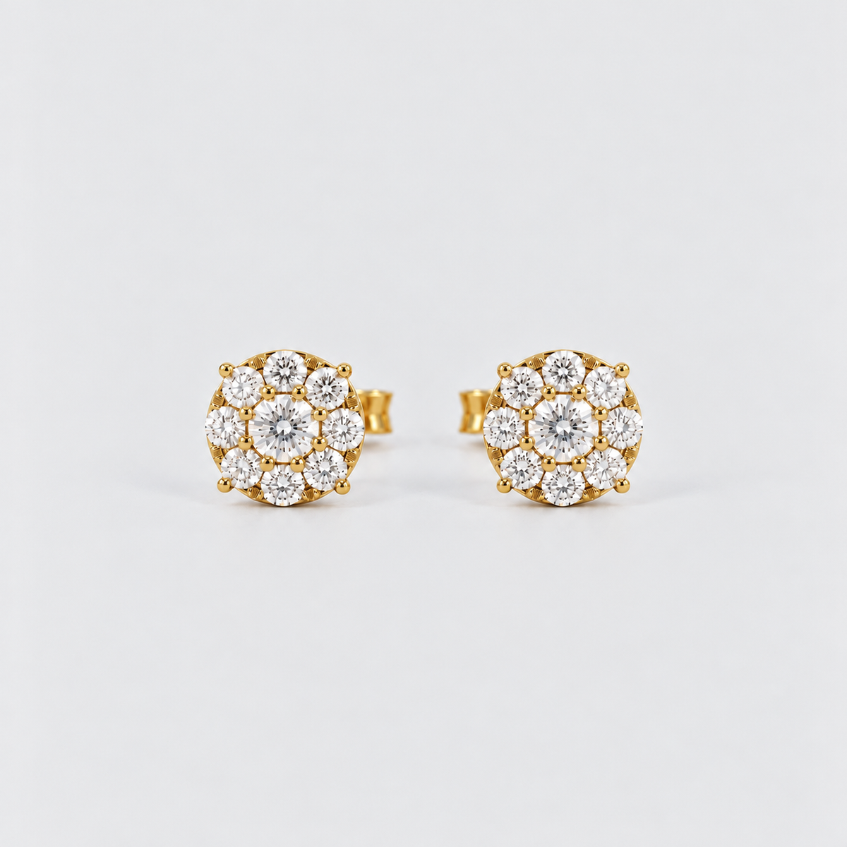 A pair of gold stud earrings with round floral clusters of clear gemstones, photographed on a clean light gray background.