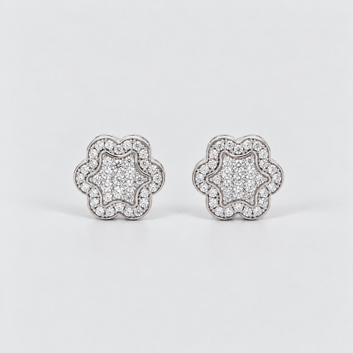 A pair of silver-toned flower-shaped stud earrings paved with clear cubic zirconia stones, displayed on a clean light gray background.