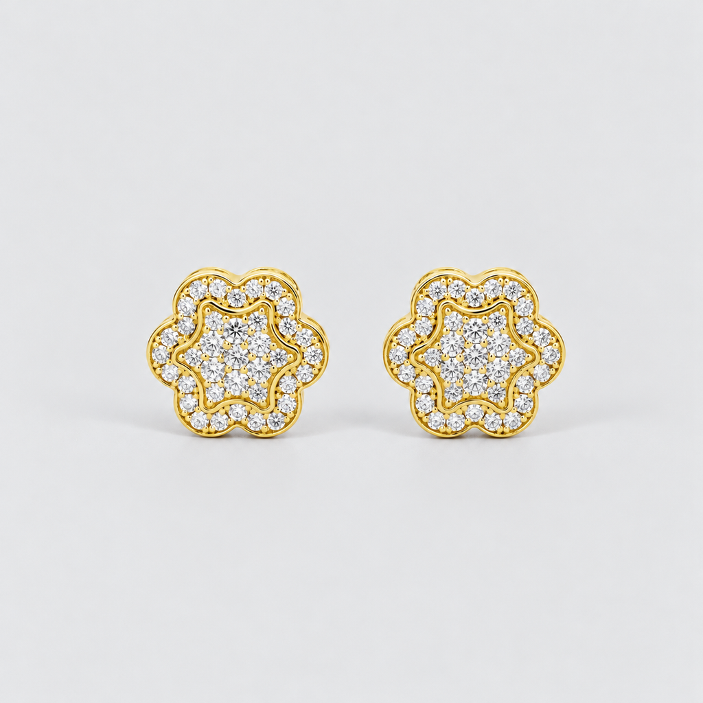 A pair of gold flower-shaped stud earrings paved with clear round stones, set against a clean light gray background.