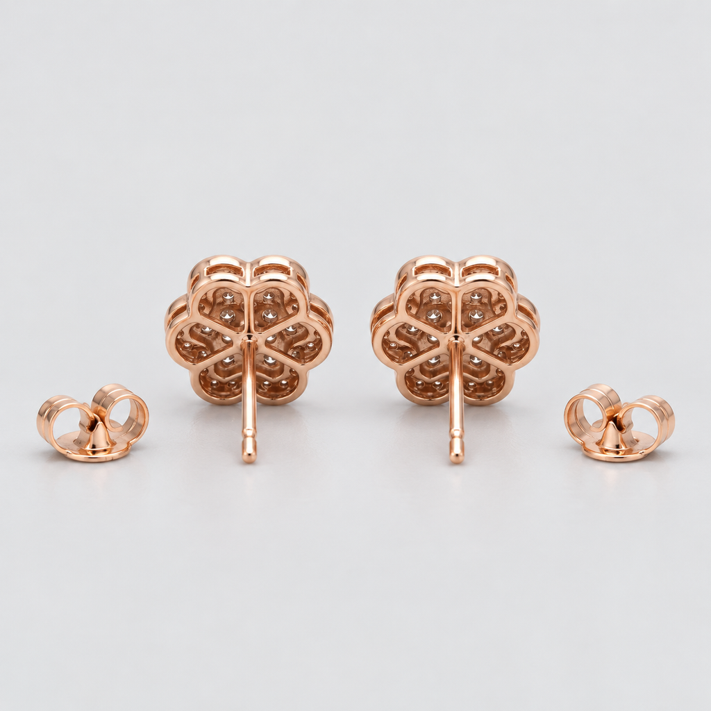 A pair of rose gold stud earrings with a four-petal flower design, shown with their butterfly backings on a light gray background.