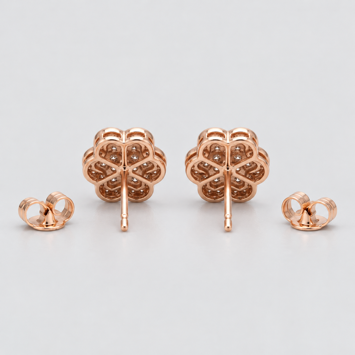 A pair of rose gold stud earrings with a four-petal flower design, shown with their butterfly backings on a light gray background.