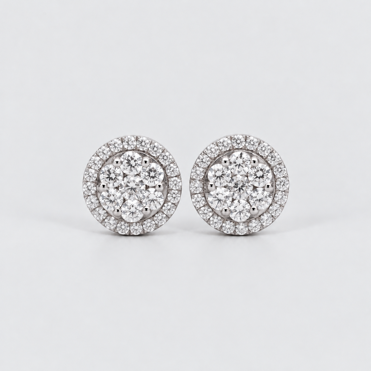 A pair of round diamond stud earrings with a double halo setting in silver-toned metal, displayed on a clean light gray background.