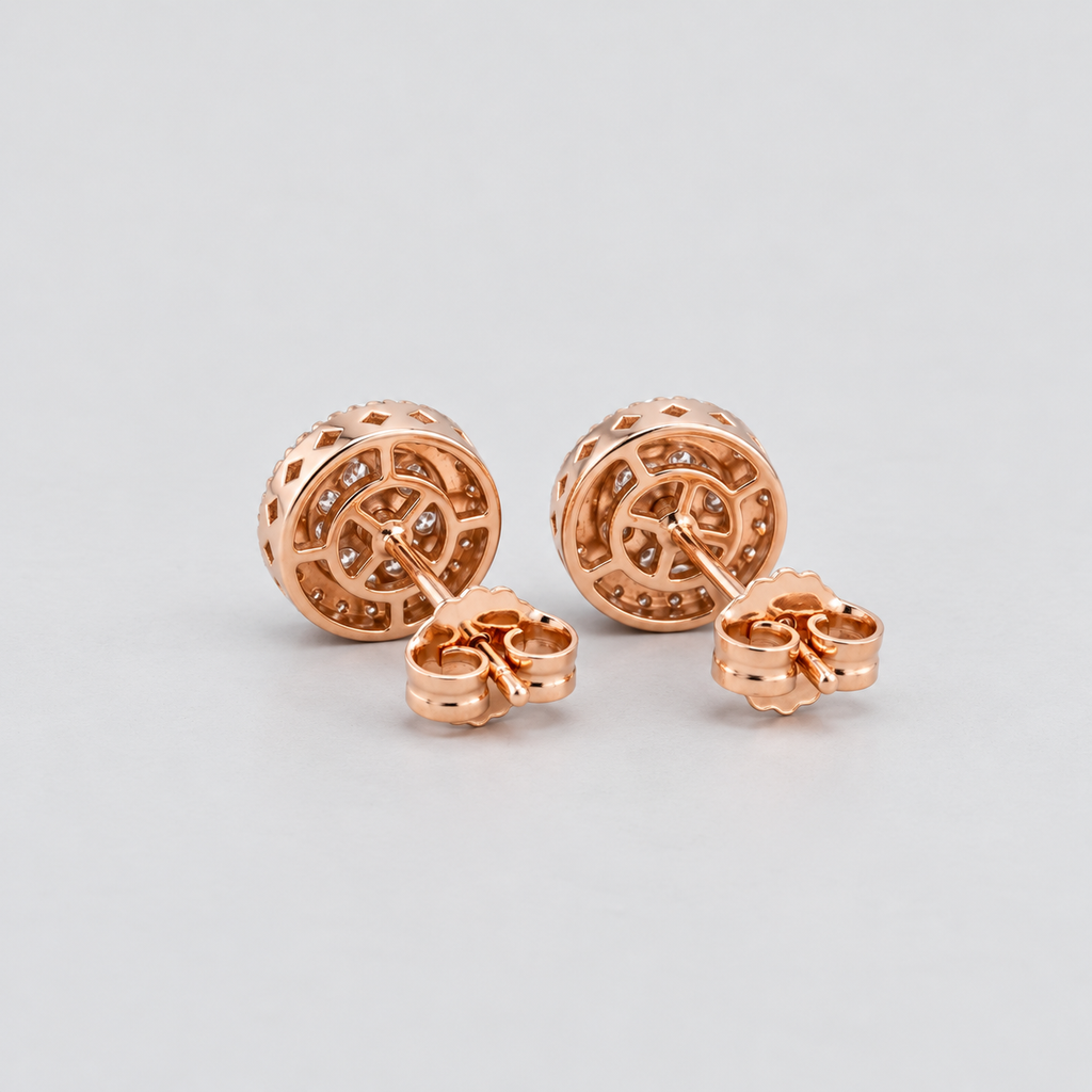 A pair of rose gold stud earrings with intricate circular filigree cutouts and small inset stones, displayed on a light gray background.