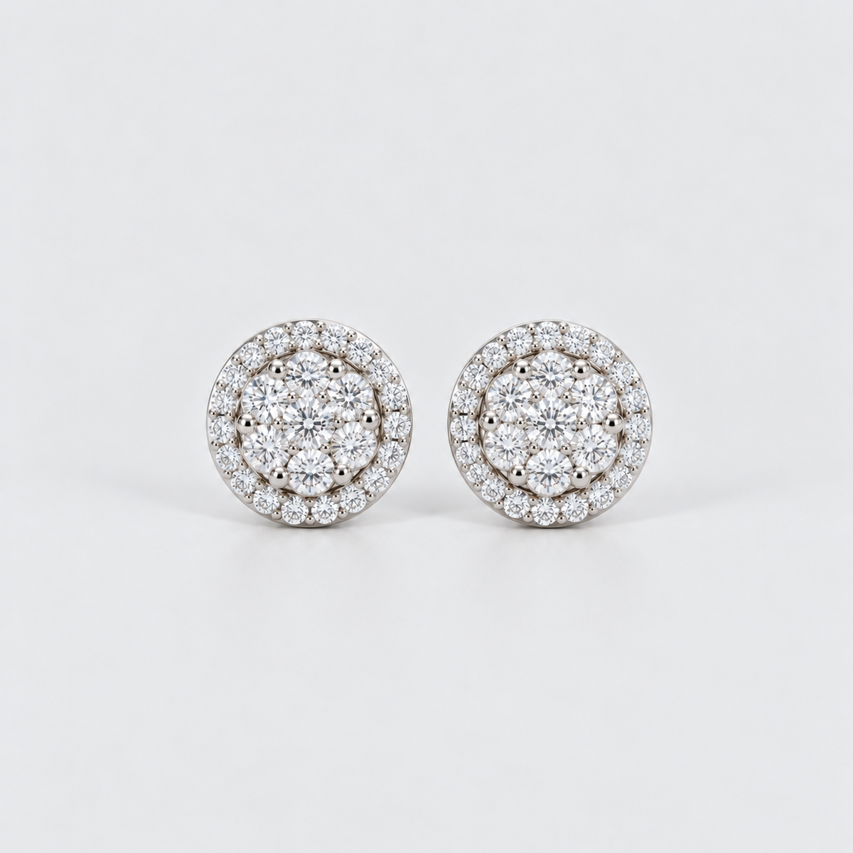 A pair of round diamond stud earrings with a double halo setting in silver-toned metal, photographed on a clean light gray background.