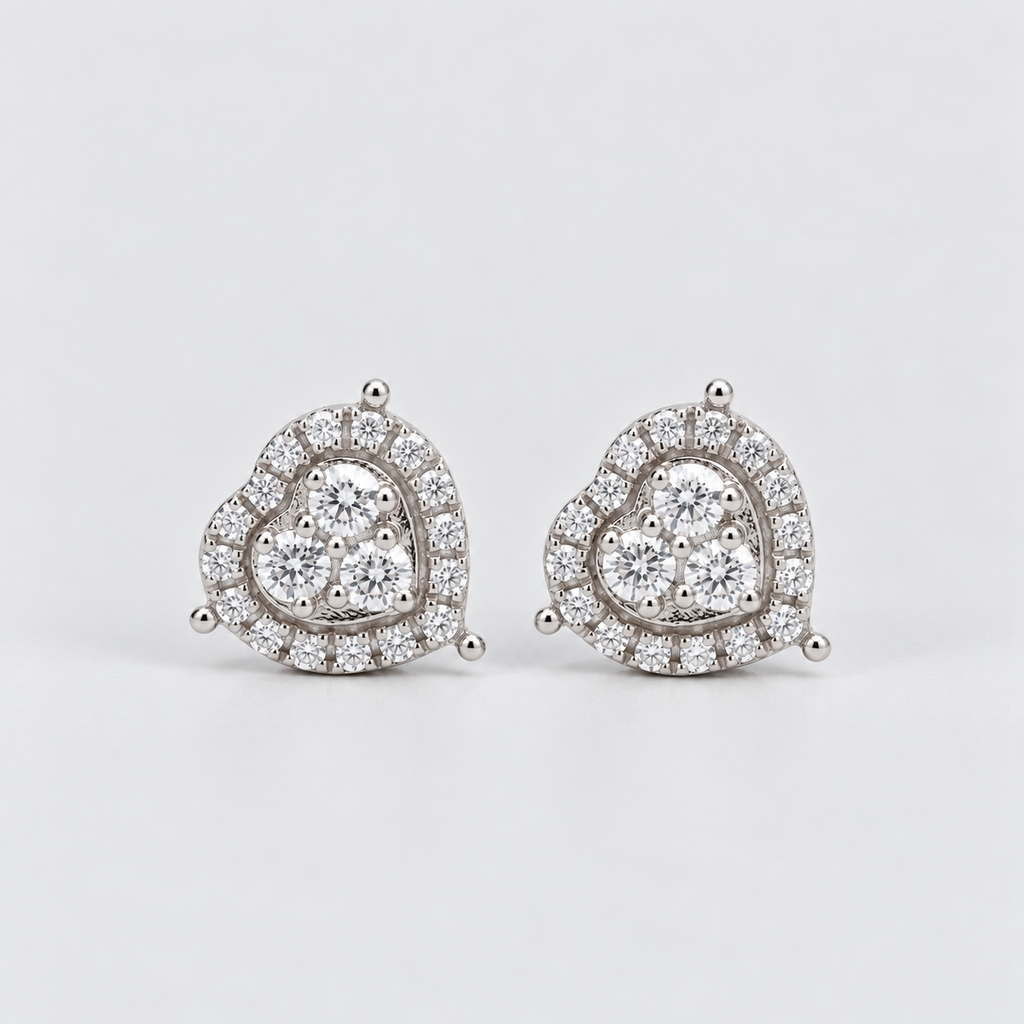 A pair of heart-shaped stud earrings in silver-tone metal, adorned with clear pavé diamonds and a central cluster of round diamonds, set against a plain light gray background.