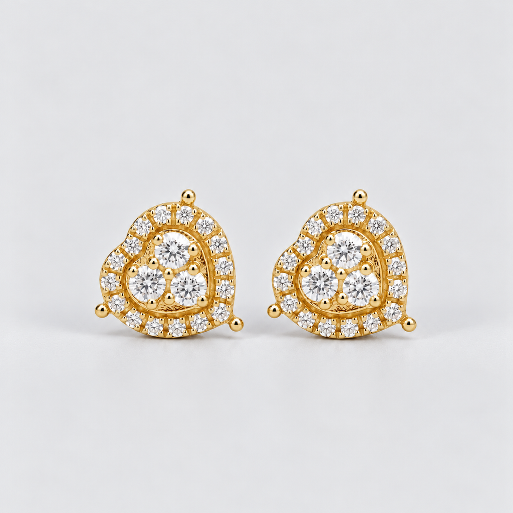 A pair of gold heart-shaped stud earrings set with clear pavé diamonds, photographed on a clean light gray background.