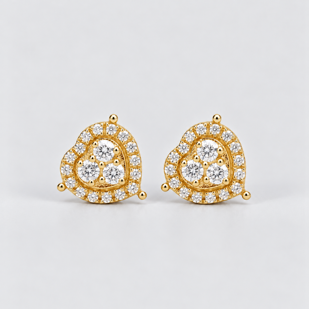 A pair of gold heart-shaped stud earrings set with clear pavé diamonds, photographed on a clean light gray background.