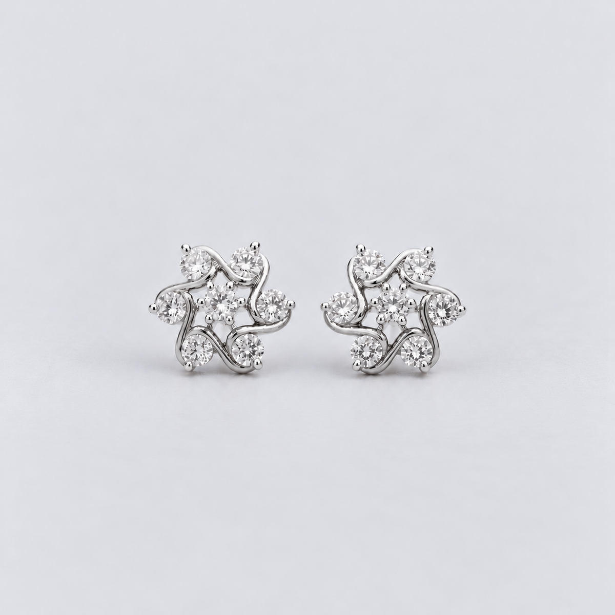 A pair of silver-toned stud earrings with a floral, leaf-like cluster design set with clear round gemstones, displayed on a light gray background.