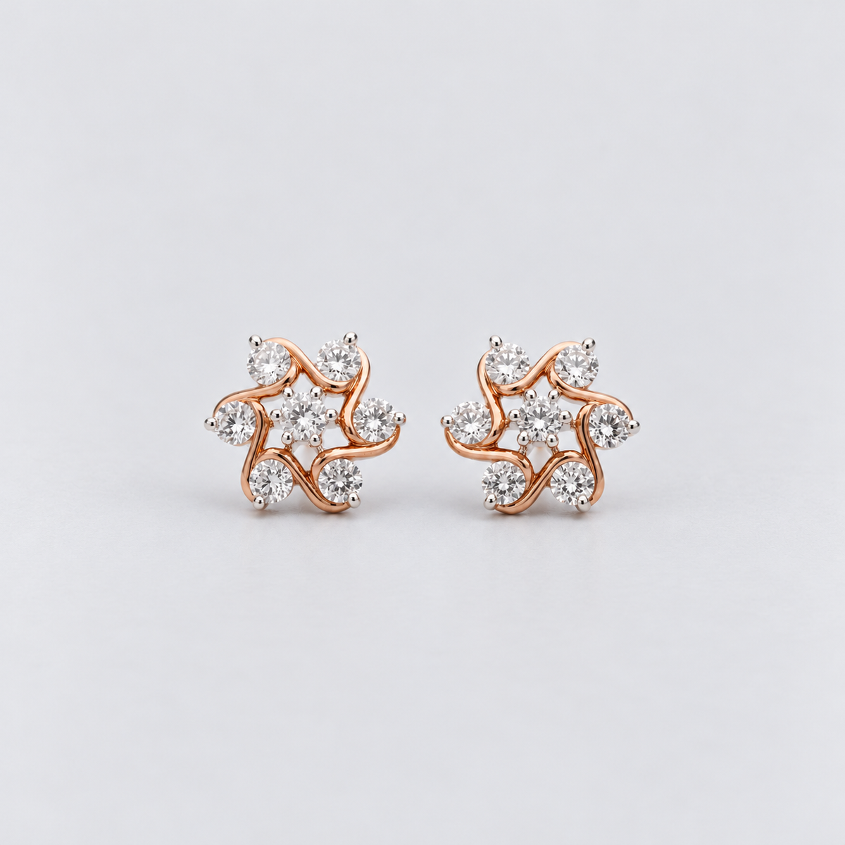 A pair of rose gold stud earrings with clear cubic zirconia stones, arranged in a swirling, abstract floral pattern on a light gray background.