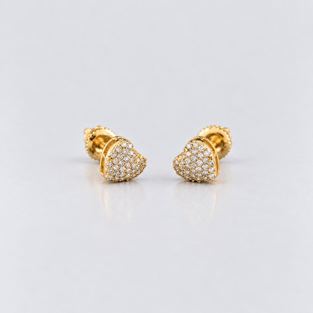 A pair of gold heart-shaped stud earrings paved with small clear stones, displayed on a light gray reflective surface.