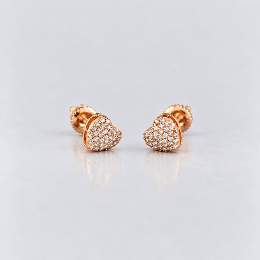 A pair of rose gold heart-shaped stud earrings paved with small clear stones, displayed on a light gray reflective surface.