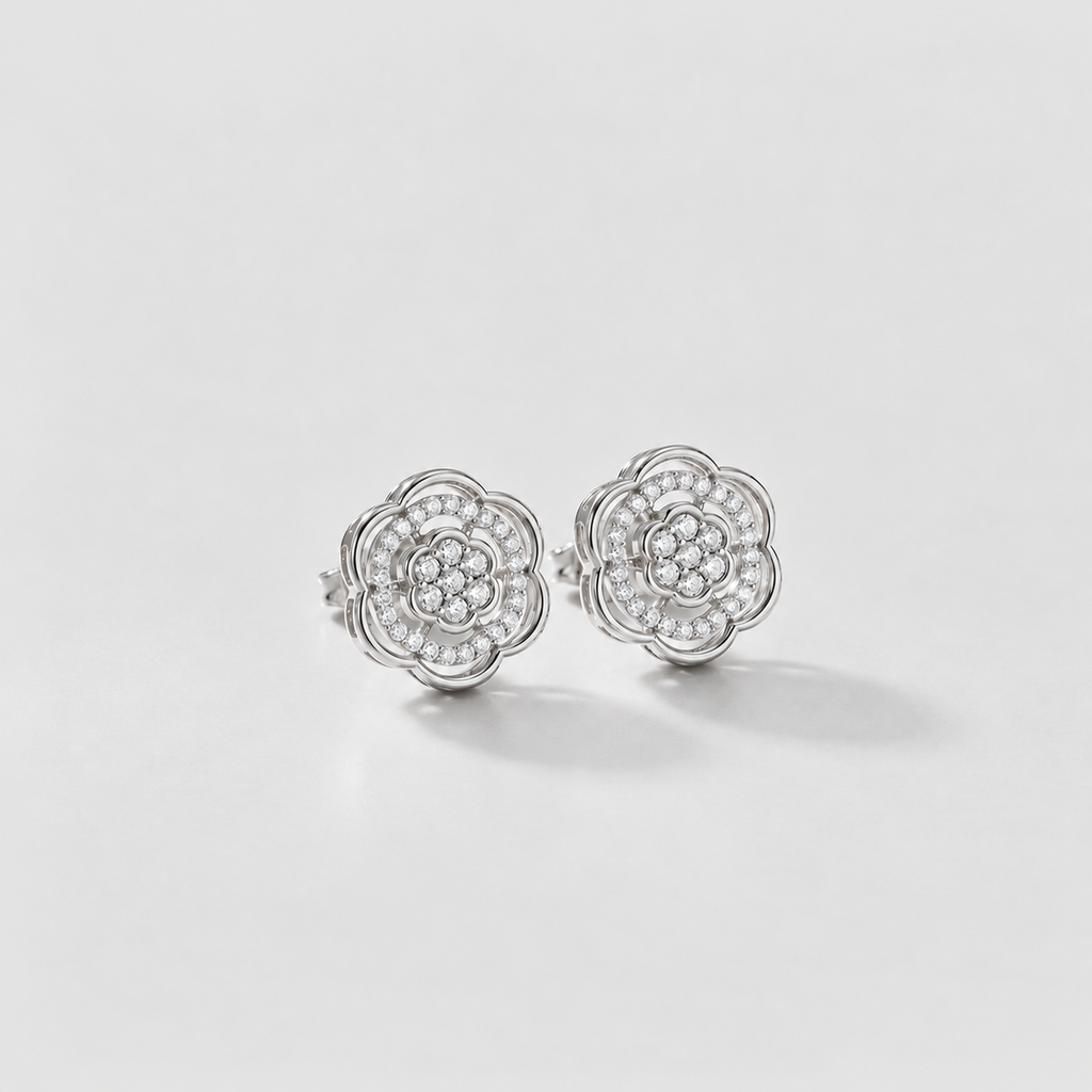 A pair of silver stud earrings with a multi-layered flower design set with small clear stones, photographed on a clean white background.
