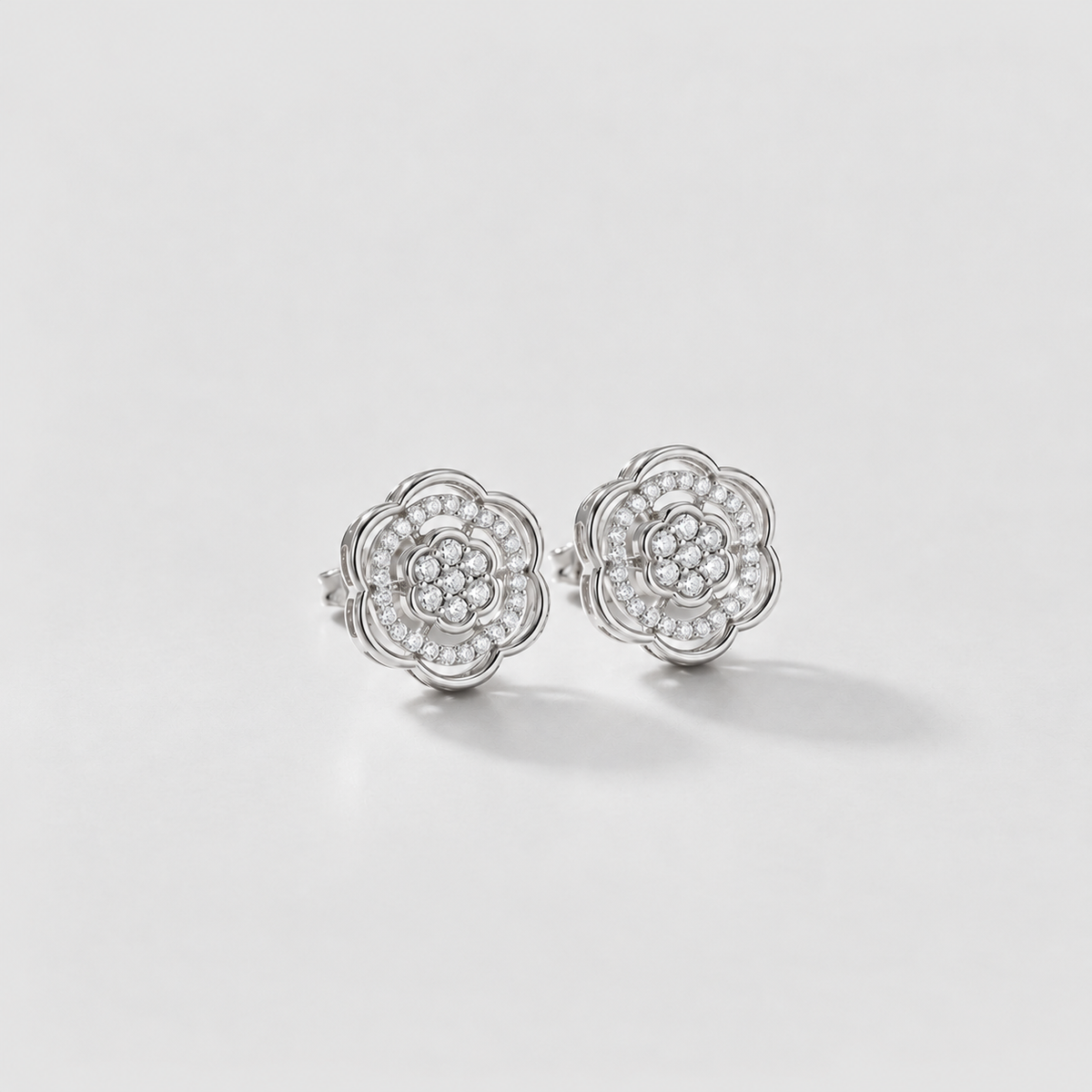 A pair of silver stud earrings with a multi-layered flower design set with small clear stones, photographed on a clean white background.