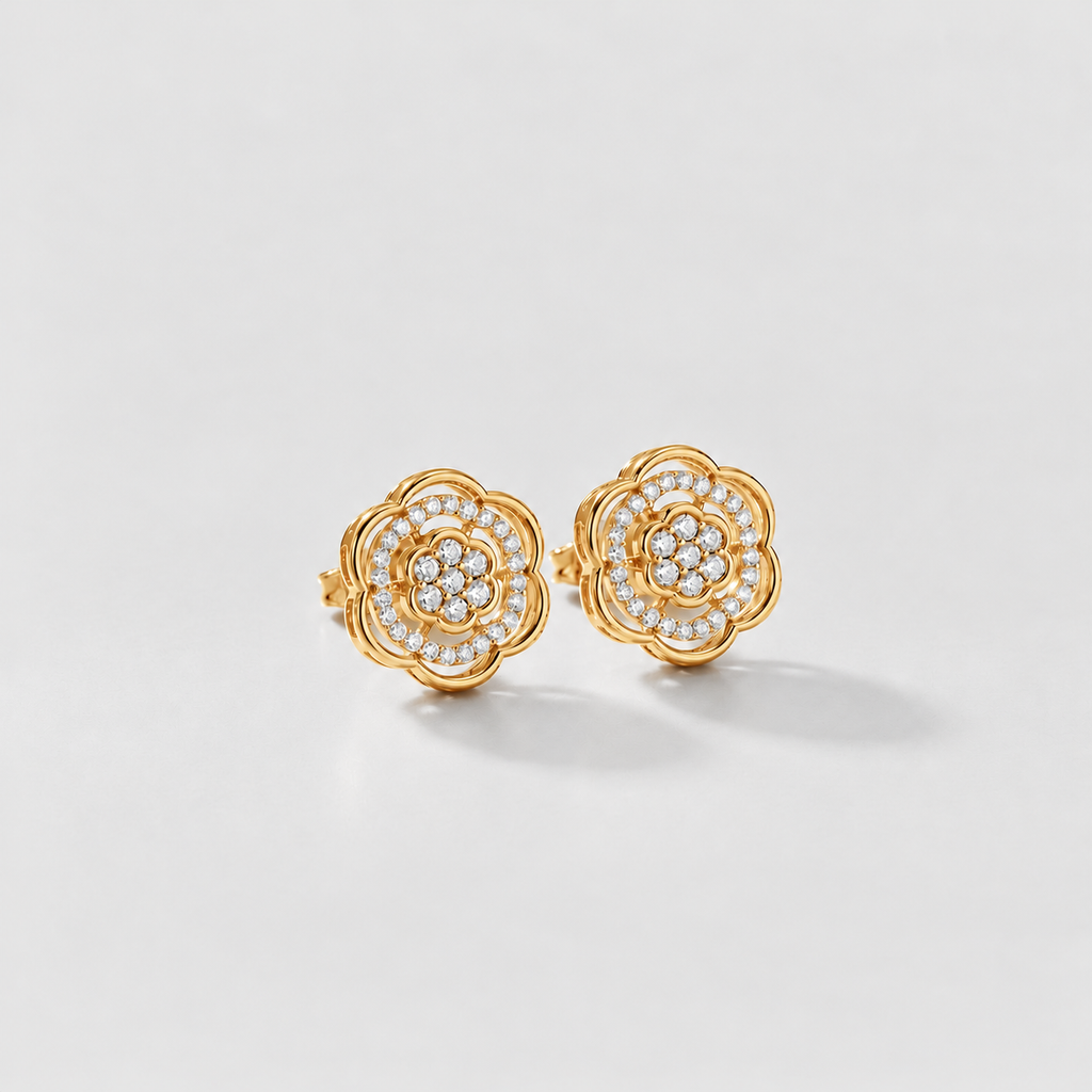 A pair of gold flower-shaped stud earrings adorned with small clear pavé stones, photographed on a clean light gray background.