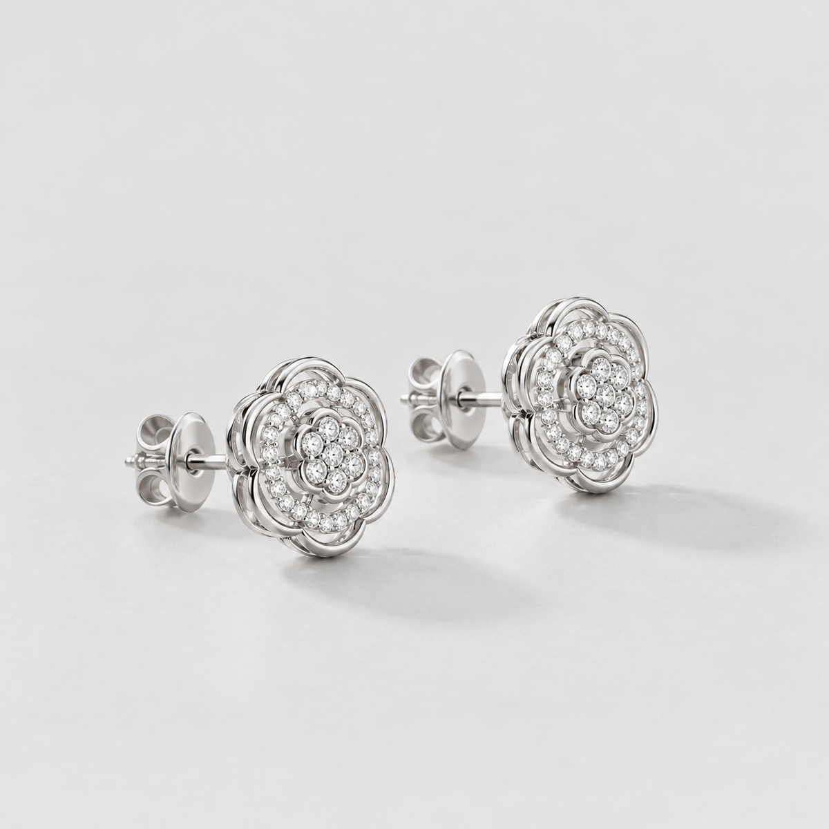 A pair of silver-toned flower-shaped stud earrings with pavé-set clear stones, displayed on a clean light gray background.
