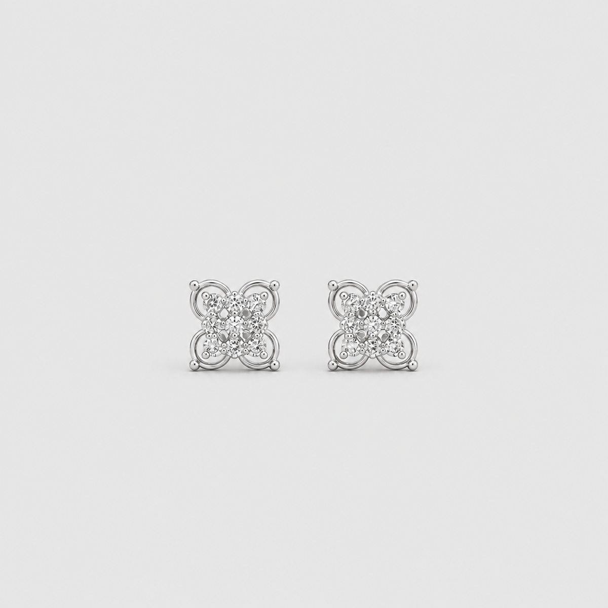 A pair of silver-toned square stud earrings with a floral or clover-like design set with small clear stones, shown on a light gray background.