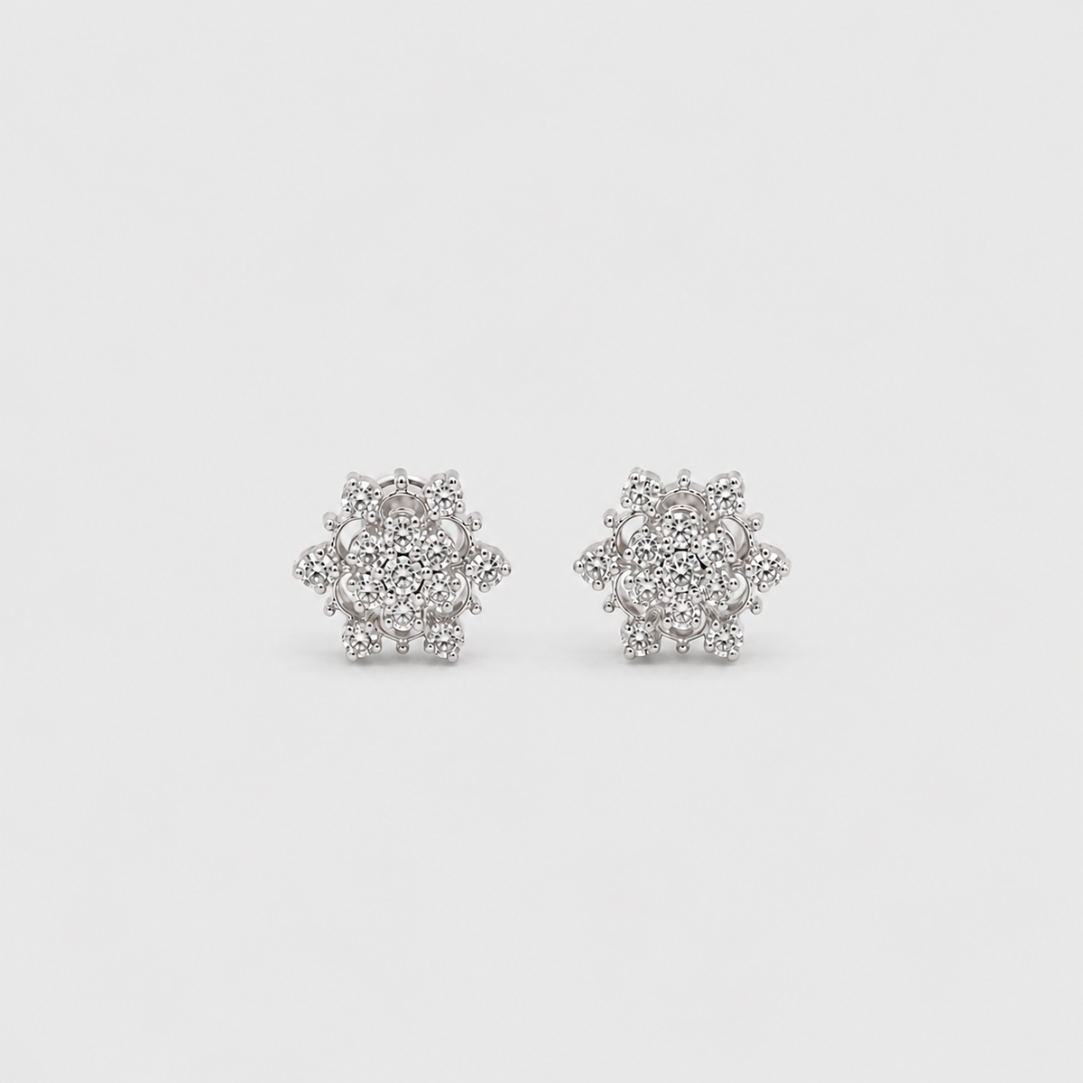 A pair of snowflake-shaped stud earrings made of silver-toned metal and clear stones, displayed on a light gray background.