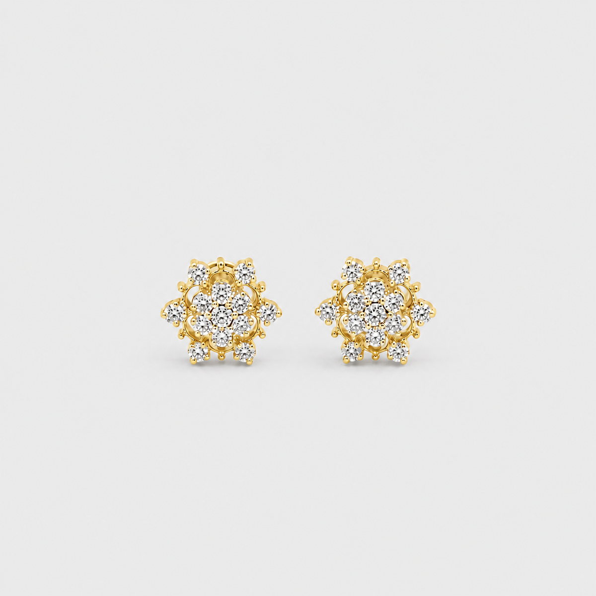 A pair of gold stud earrings with round cluster pavé settings set with clear stones, displayed on a light gray background.
