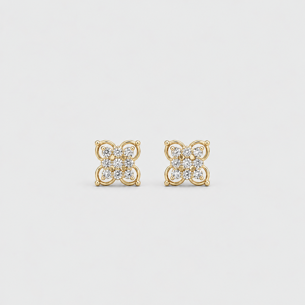 A pair of gold stud earrings with a four-petal flower design set with small clear gemstones, shown on a light gray background.
