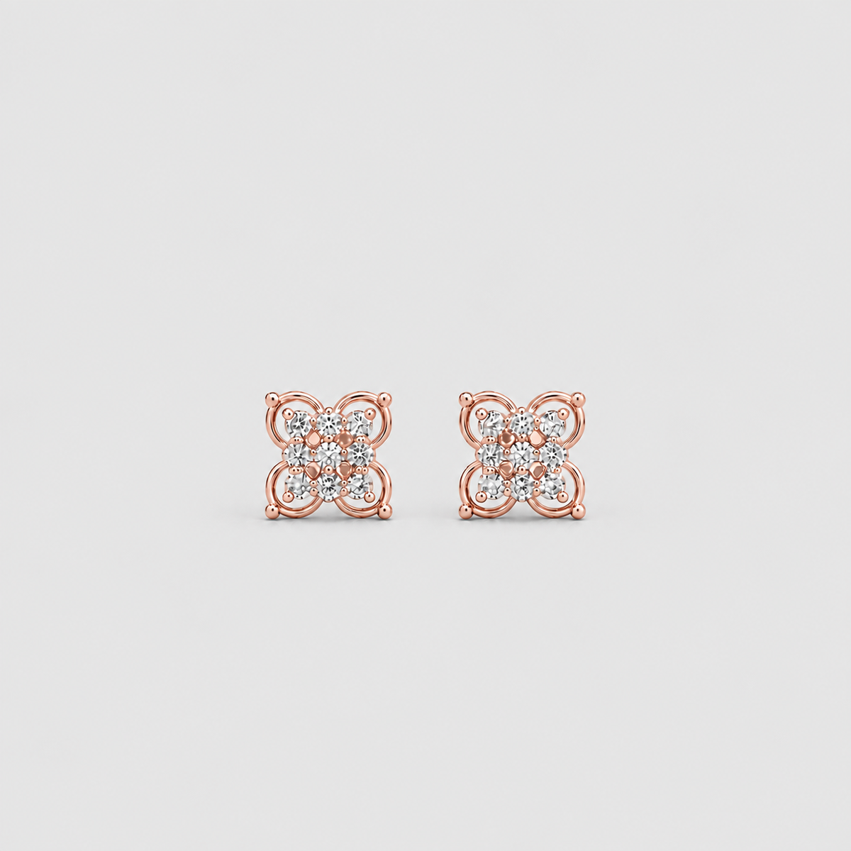 A pair of rose gold stud earrings with a square floral design set with small clear gemstones, shown on a light gray background.