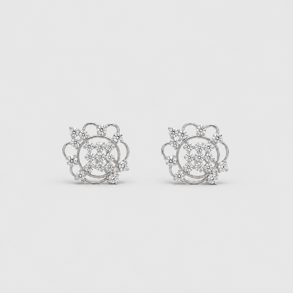 A pair of silver-toned stud earrings with intricate circular and floral designs set with clear gemstones, displayed on a light gray background.