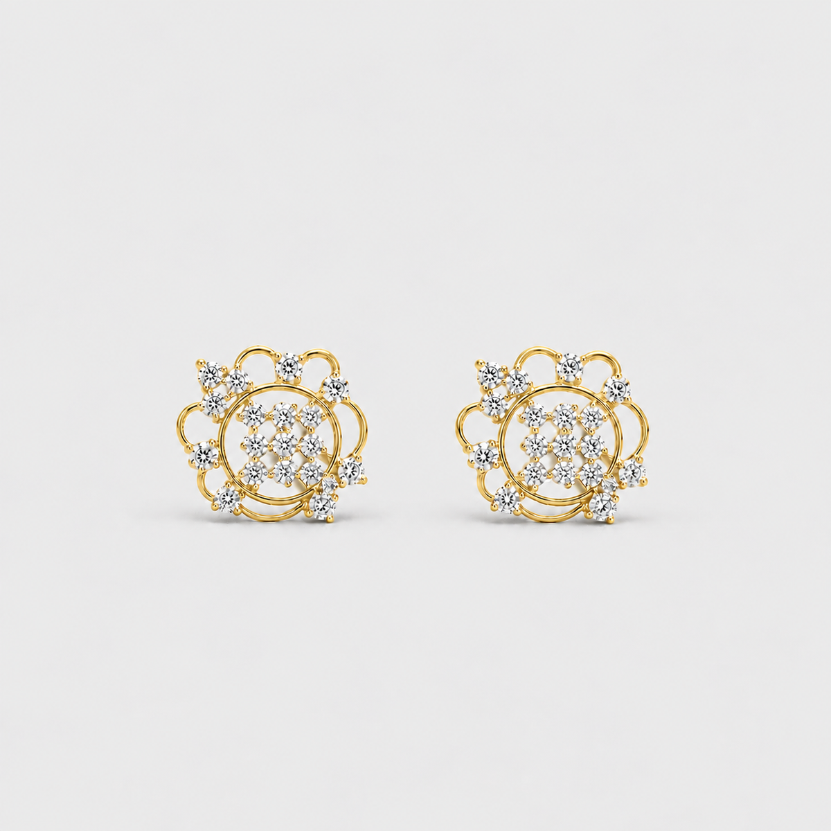 A pair of gold stud earrings with a circular floral design set with clear pavé gemstones, shown on a light gray background.