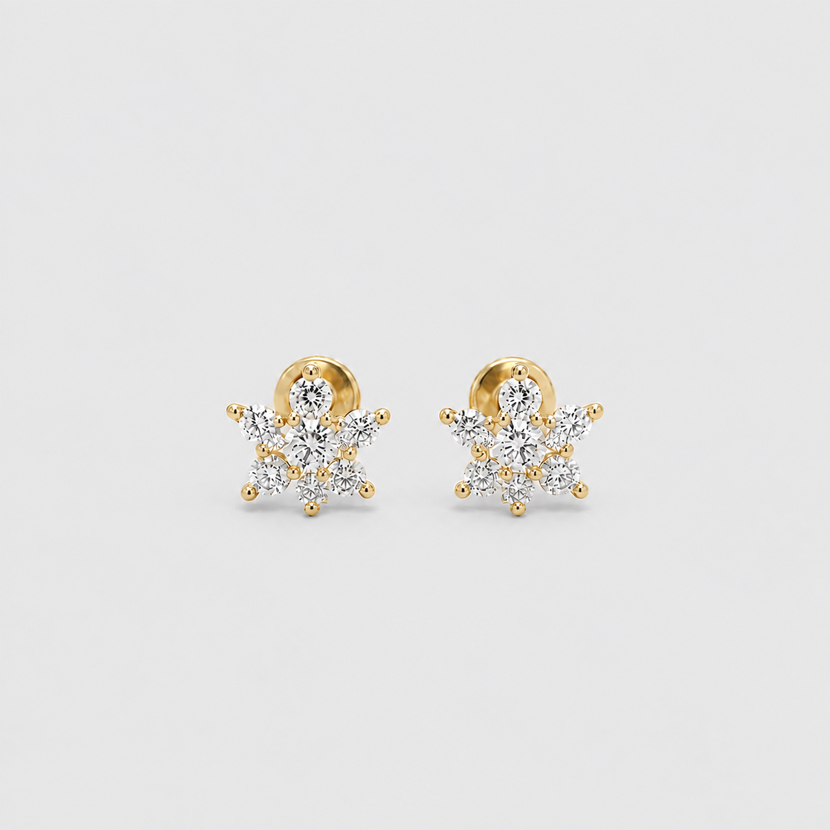 A pair of gold snowflake stud earrings set with clear gemstones, displayed on a clean light gray background.