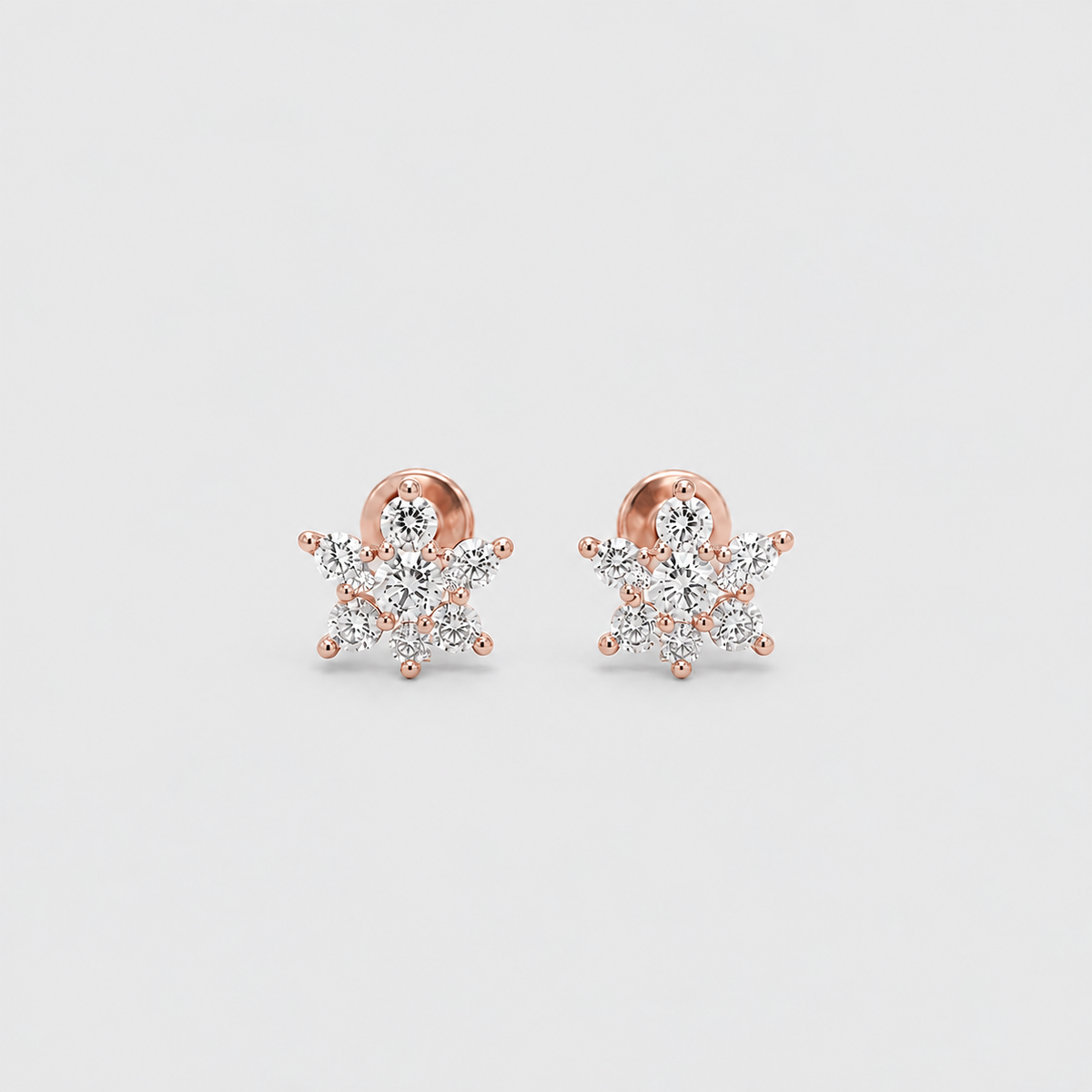 A pair of rose gold snowflake stud earrings with clear gemstones, displayed on a light gray background.