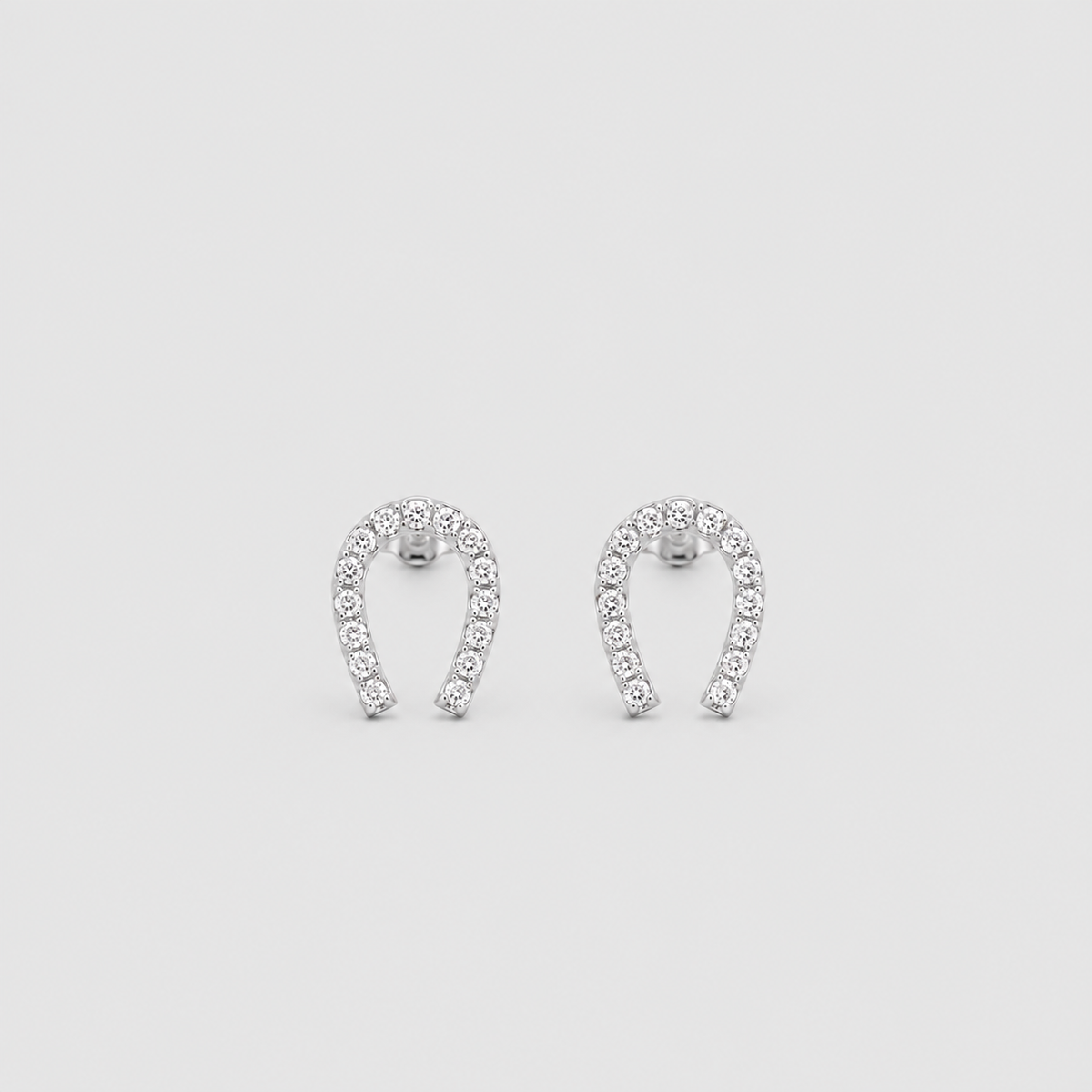 A pair of silver horseshoe-shaped stud earrings set with small clear stones, displayed on a light gray background.