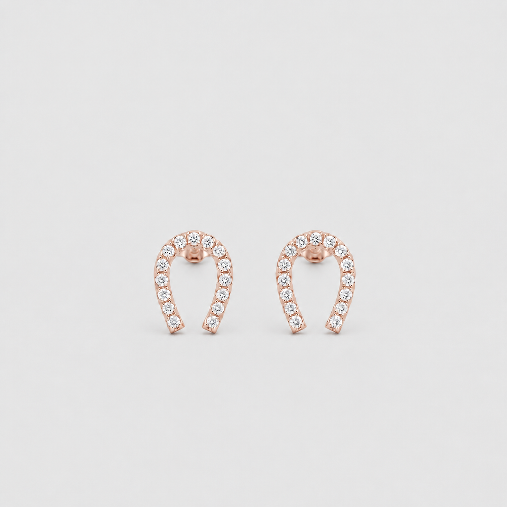 A pair of rose gold horseshoe-shaped stud earrings set with small clear stones, displayed on a light gray background.