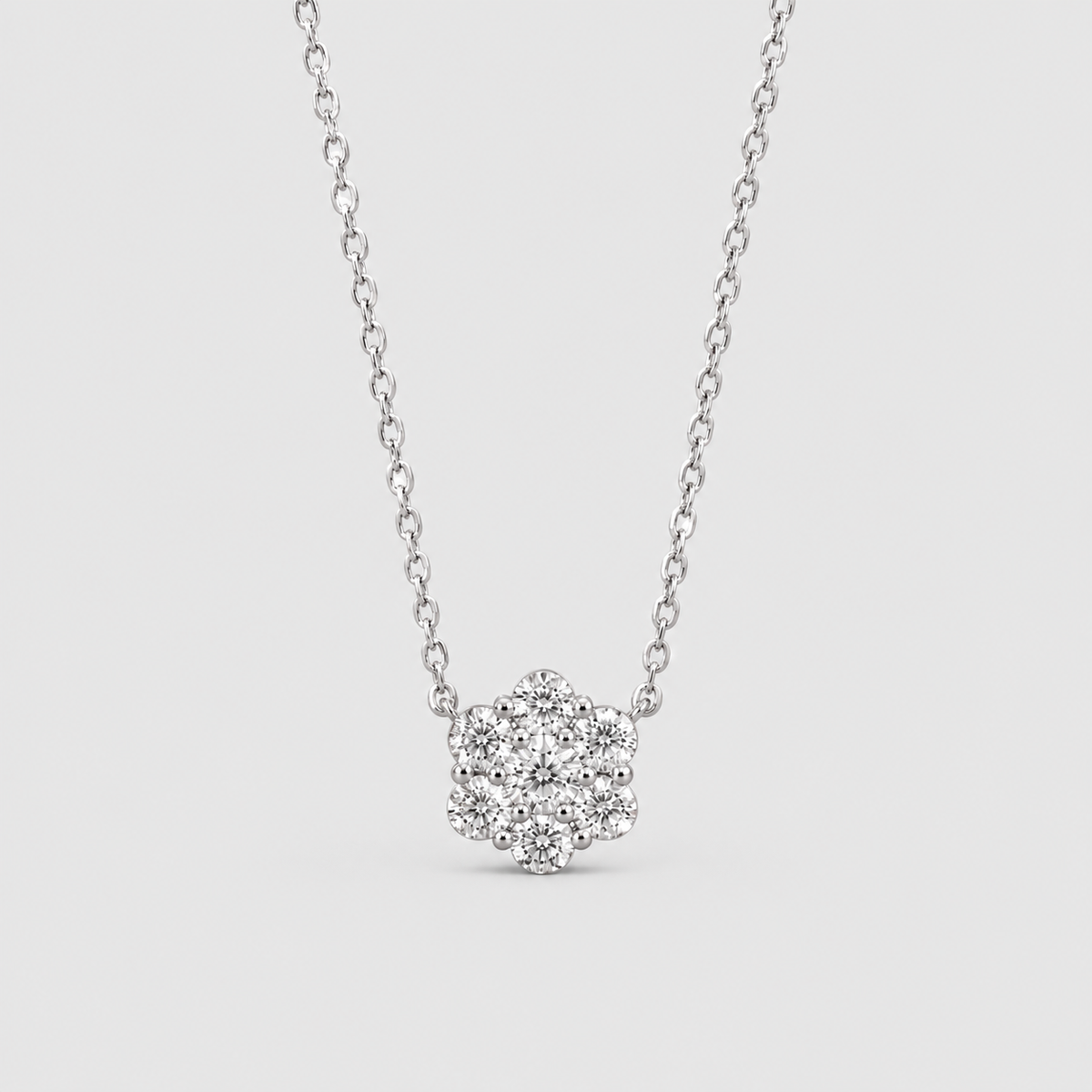 A silver-toned necklace with a small flower-shaped cluster of clear stones on a delicate chain, shown against a light gray background.