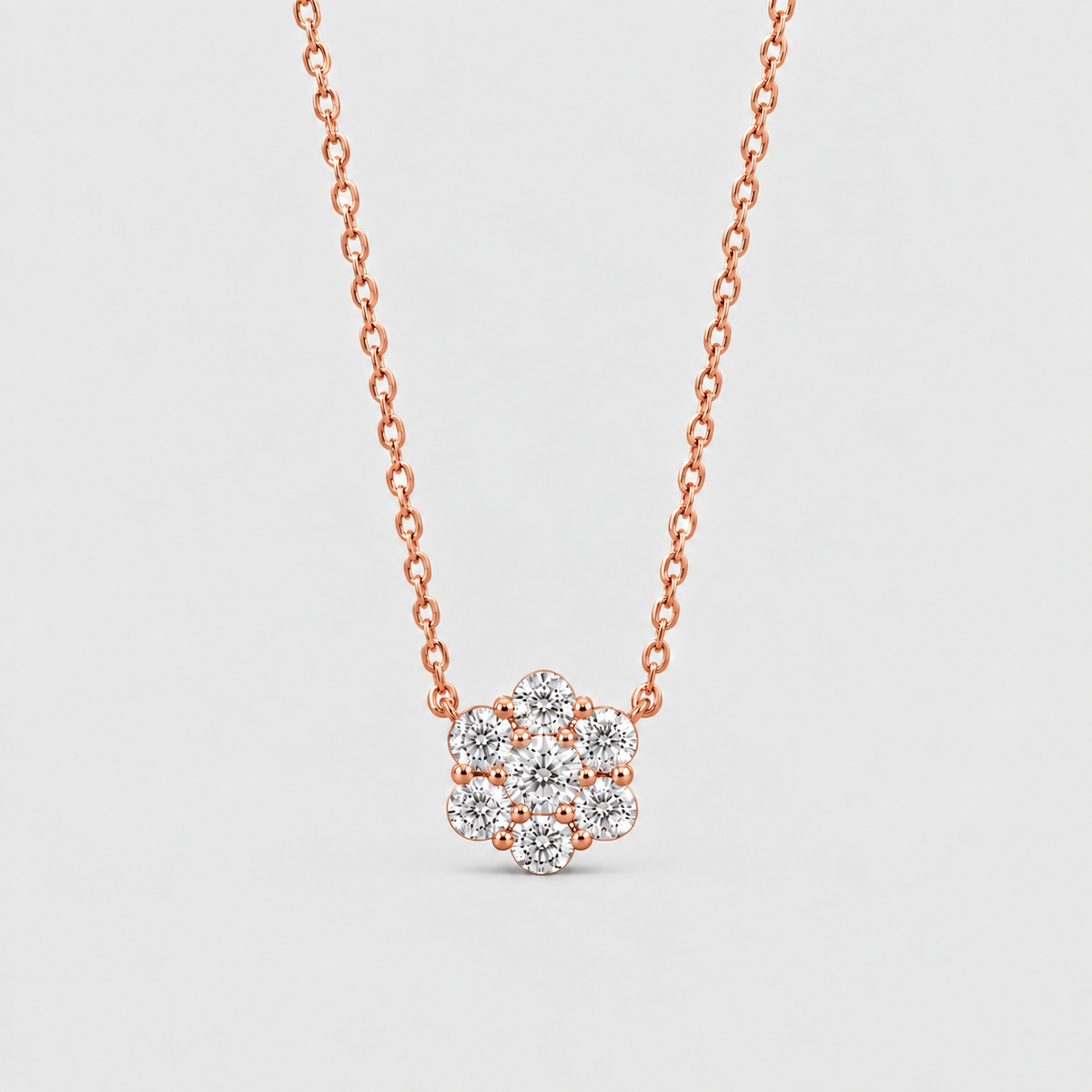 A rose gold chain necklace with a small flower-shaped cluster of clear gemstones, shown against a light gray background.