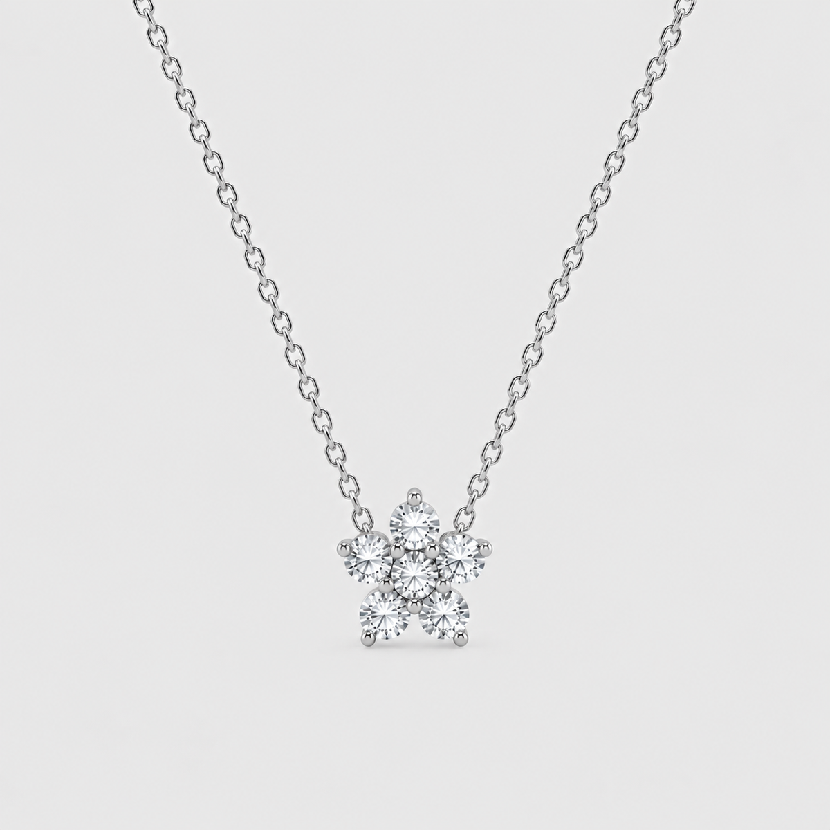 A delicate silver chain necklace with a small snowflake-shaped cluster of clear gemstones on a light gray background.