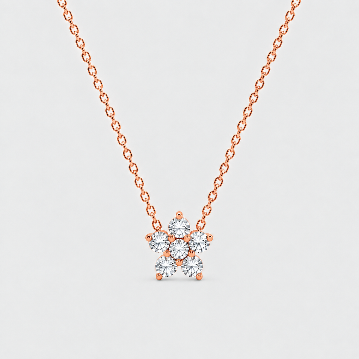 A rose gold necklace with a delicate chain and a small flower-shaped pendant set with clear round-cut gemstones, shown against a light gray background.