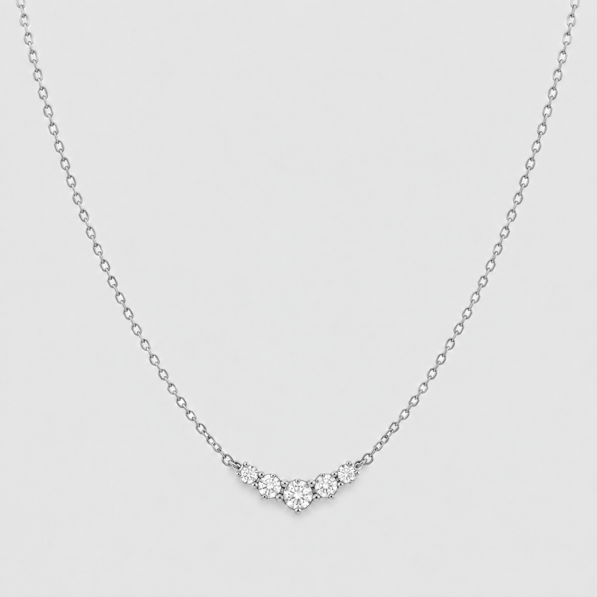 A delicate silver chain necklace featuring a small V-shaped cluster of clear round-cut gemstones at the center, set against a light gray background.