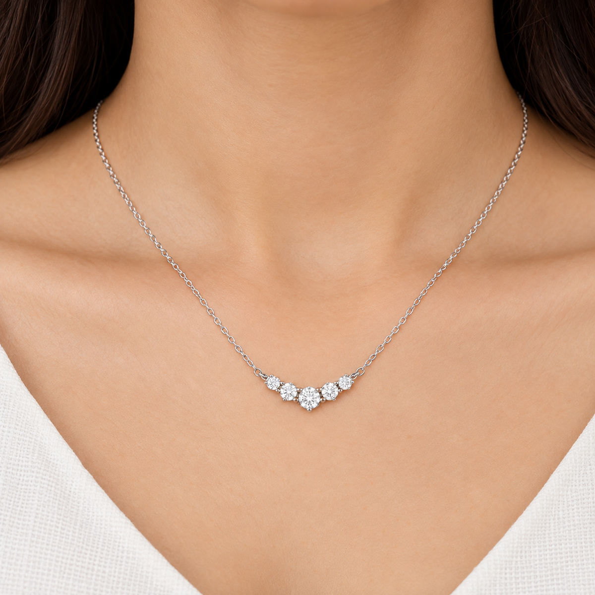 A close-up of a delicate silver chain necklace with three small clear gemstone clusters, worn on a model's neck.