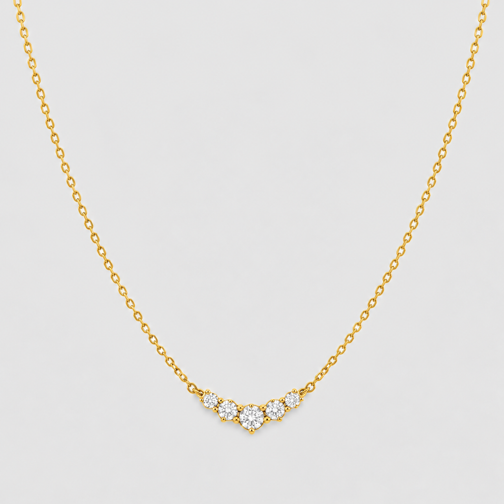A delicate gold chain necklace featuring a small V-shaped pendant with clear round-cut gemstones, displayed against a light gray background.