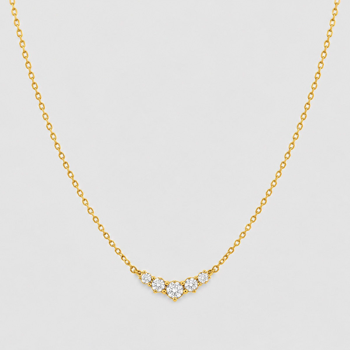 A delicate gold chain necklace featuring a small V-shaped pendant with clear round-cut gemstones, displayed against a light gray background.