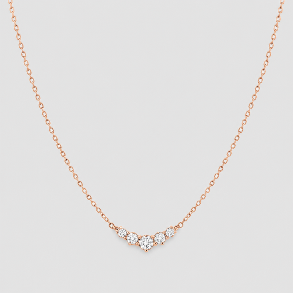 A delicate rose gold chain necklace with a small curved cluster of clear gemstones at the center, displayed against a light gray background.