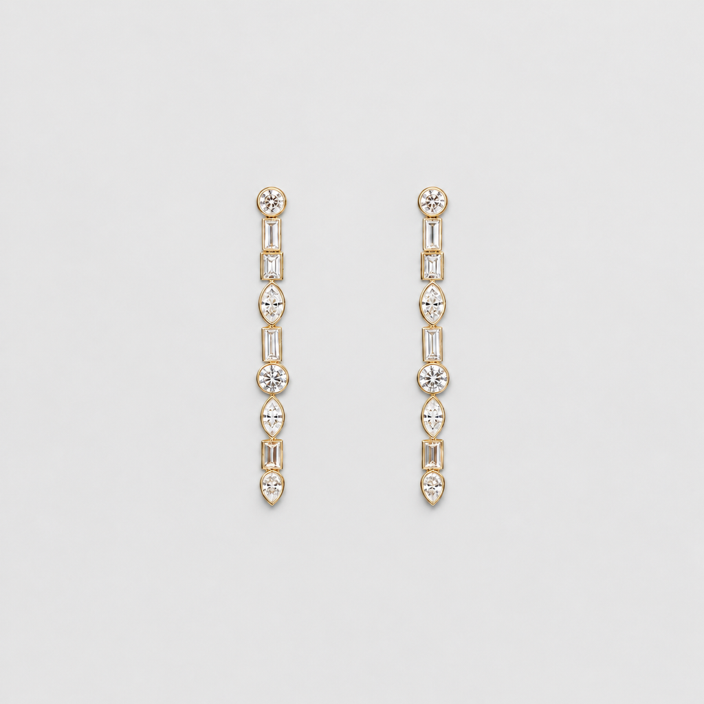 A pair of gold drop earrings with a vertical line of clear gemstones in round, baguette, and marquise shapes, set against a light gray background.