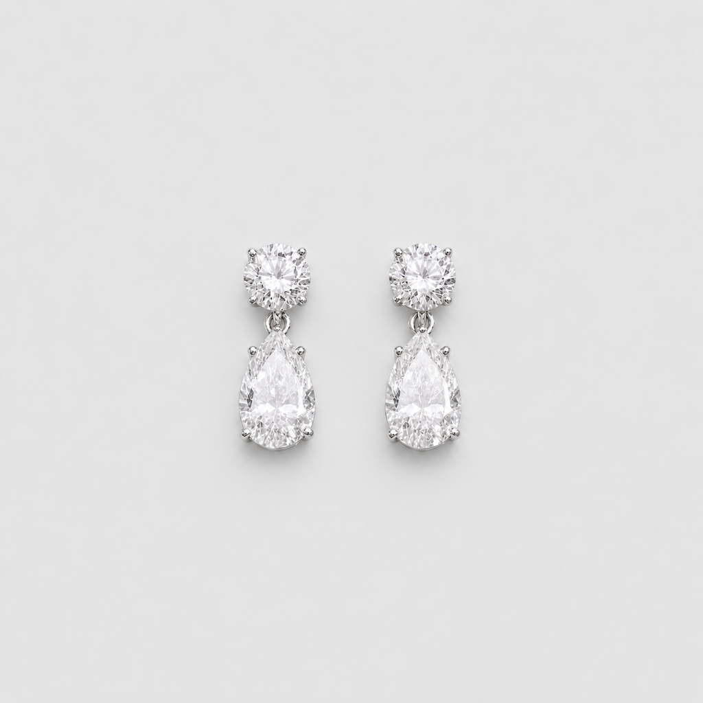 A pair of silver drop earrings featuring a round-cut clear gemstone at the top and a pear-cut clear gemstone below, set against a light gray background.